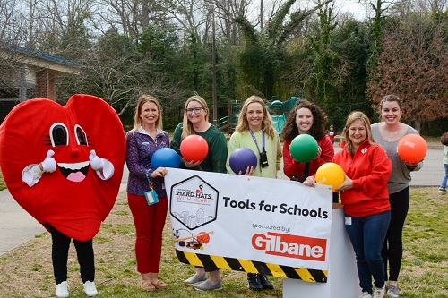 Heart mascot with group of six women holding rainbow colored athletic balls and banner reading Tools for schools sponsored by Gilbane.